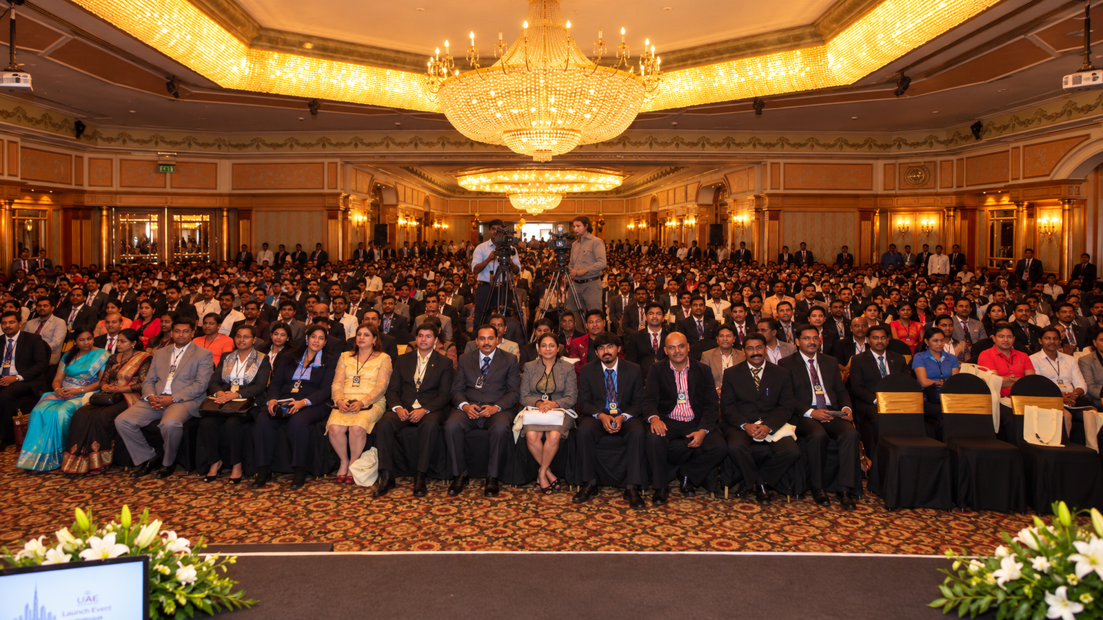 View from the stage of the packed Falcon Ballroom, rows of attendees with lanyards, chandeliers overhead