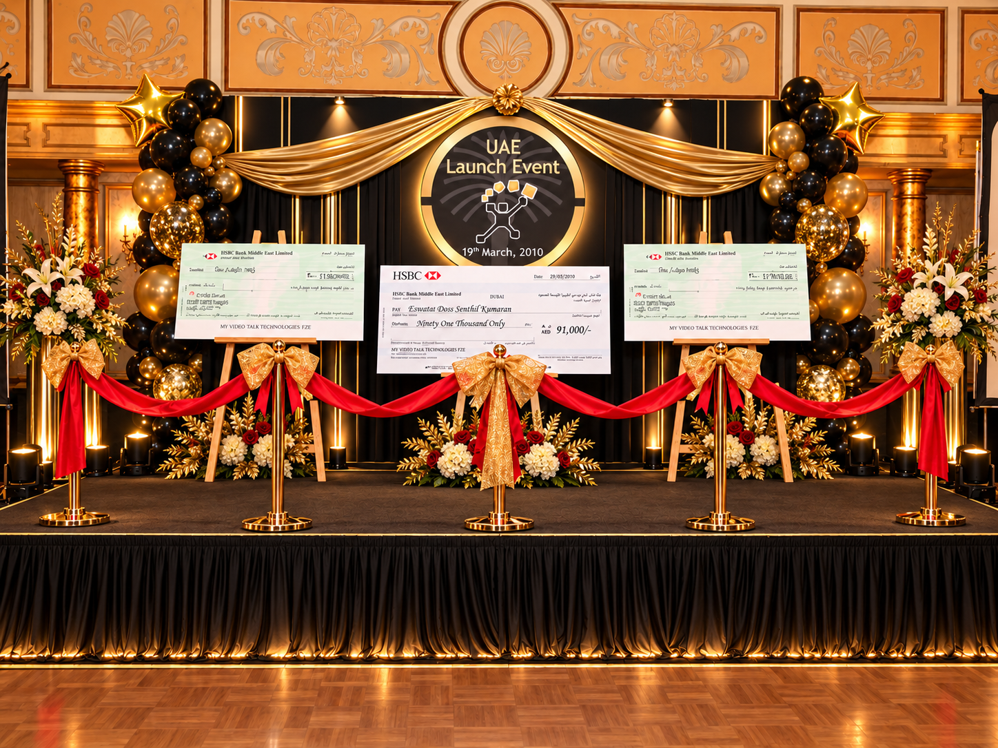 The Falcon Ballroom stage decorated in gold and black, with three enlarged HSBC cheques displayed on easels beneath the UAE Launch Event, 19th March 2010 backdrop